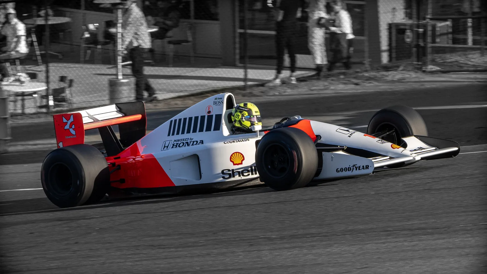 A white, red, and black open-wheel race car with Shell and Honda markings drives on a paved track.