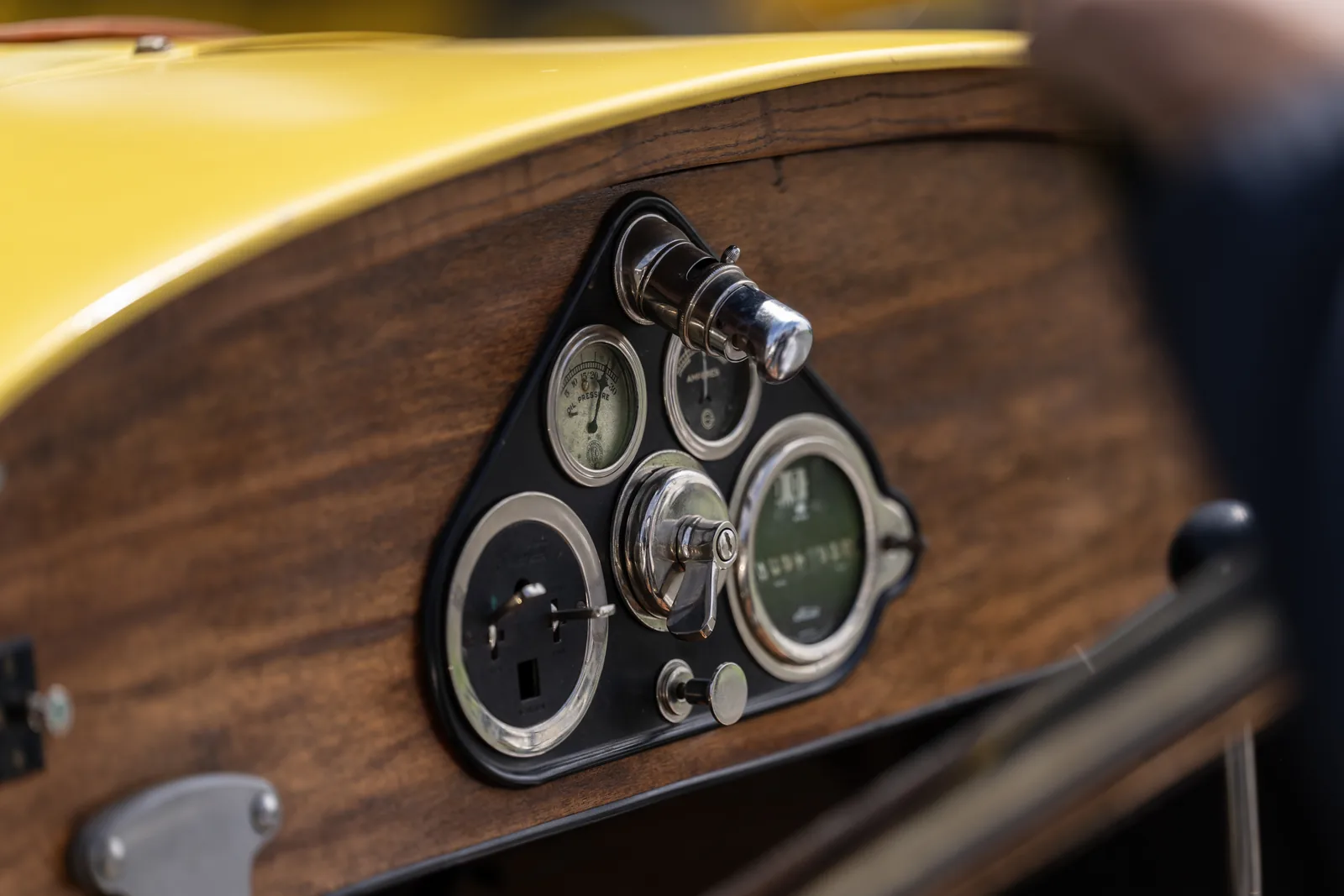 Round gauges and metal switches set into a polished wooden dashboard beneath yellow bodywork.