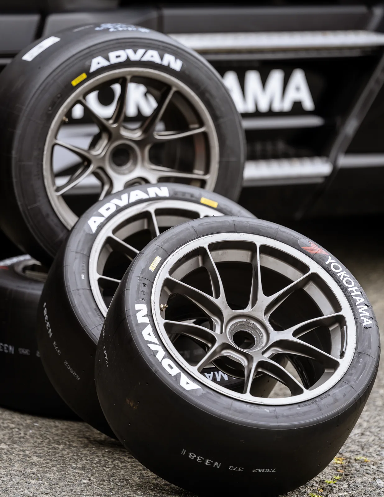 Three mounted ADVAN racing tires lean against one another beside a black Yokohama paddock barrier.