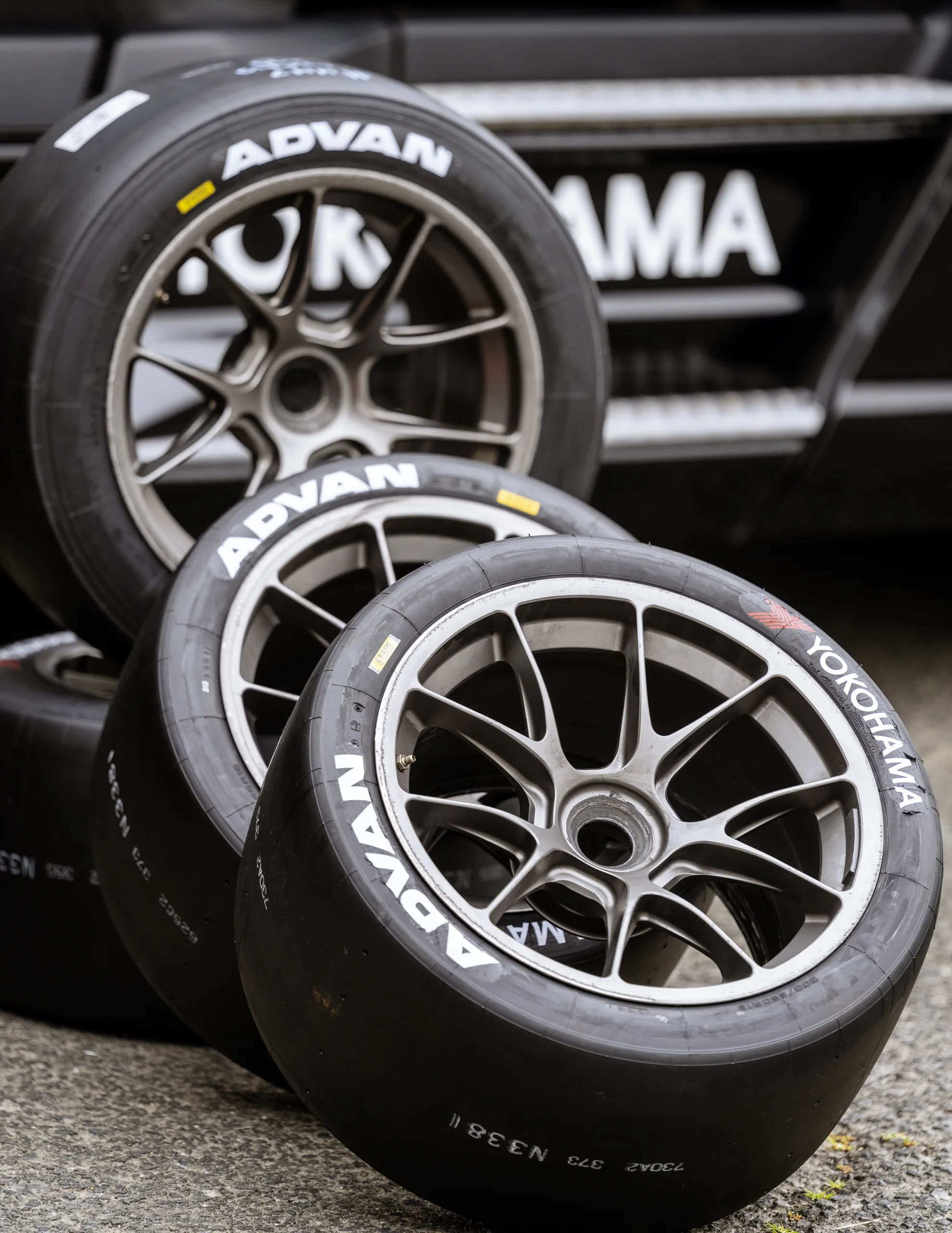 Three mounted ADVAN racing tires lean against one another beside a black Yokohama paddock barrier.